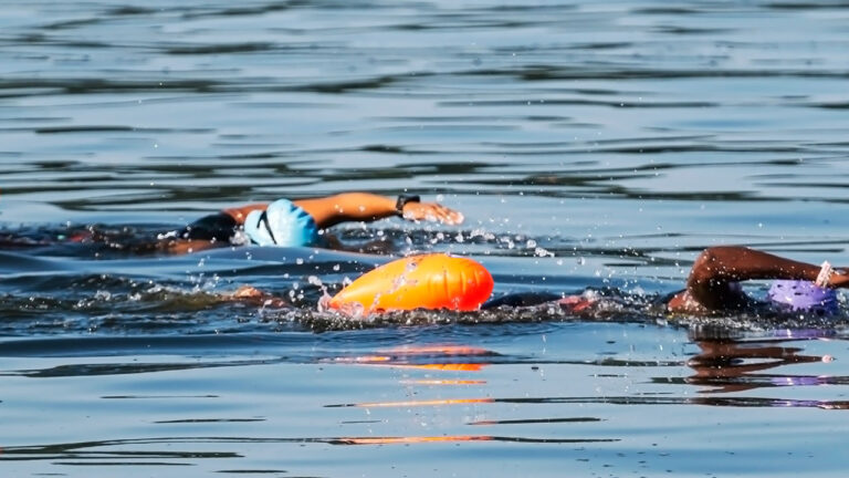 Two women swimming in cold water with safety gear