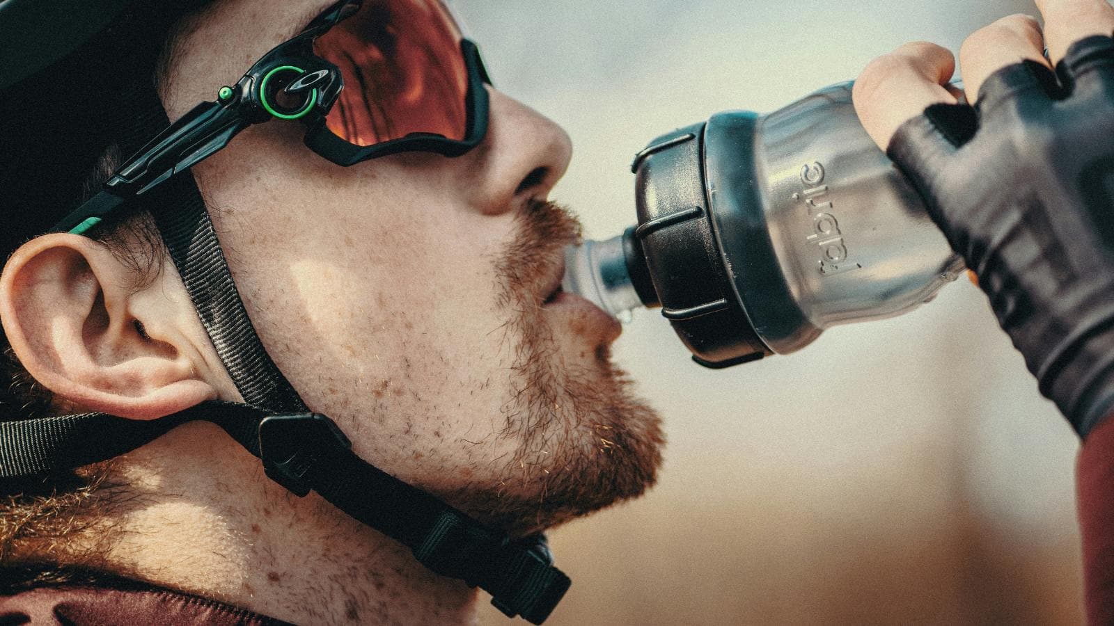 A focused triathlete wearing a bike helmet drinks an electrolyte beverage while racing, highlighting the importance of hydration and electrolyte balance during endurance sports.