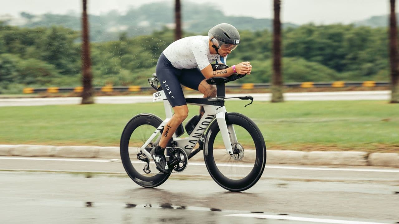 Triathlete slowing down before a wet corner using controlled braking techniques to maintain traction in rainy conditions.