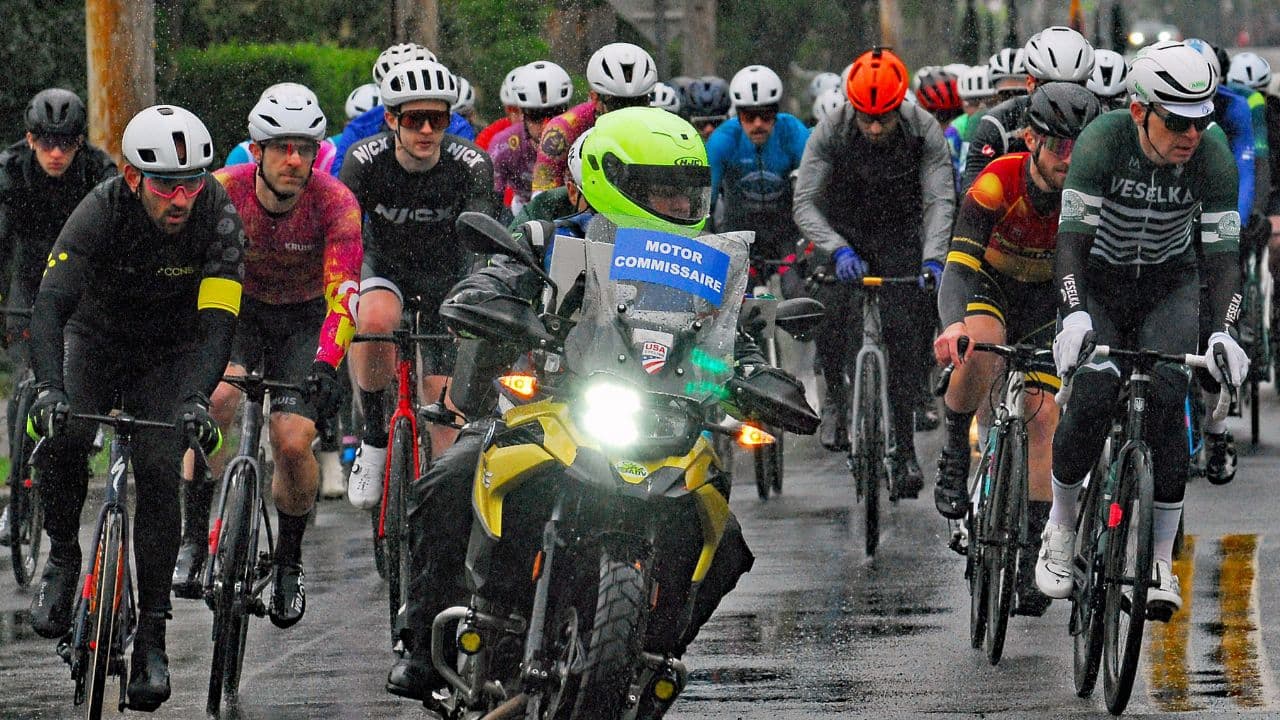 Road cyclist wearing waterproof cycling gear while riding safely on a wet road during rainy weather.