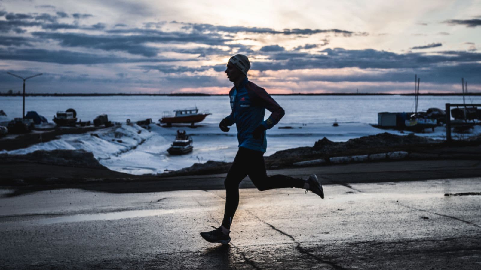 Triathlete running outdoors in cold weather wearing thermal running gear, gloves, and a hat to stay warm during winter training.