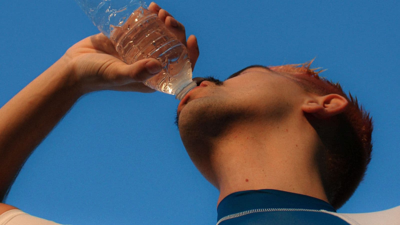 Triathlete drinking from a water bottle during the bike leg of an Ironman triathlon to prevent dehydration and maintain performance.