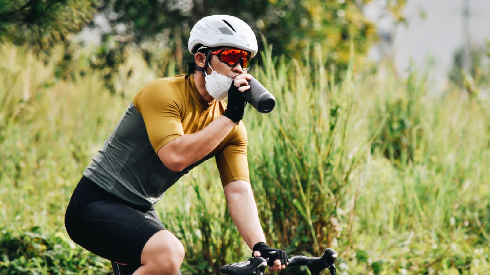 Triathlete drinking water from a cycling bottle during a hot-weather ride to stay hydrated and maintain endurance performance.