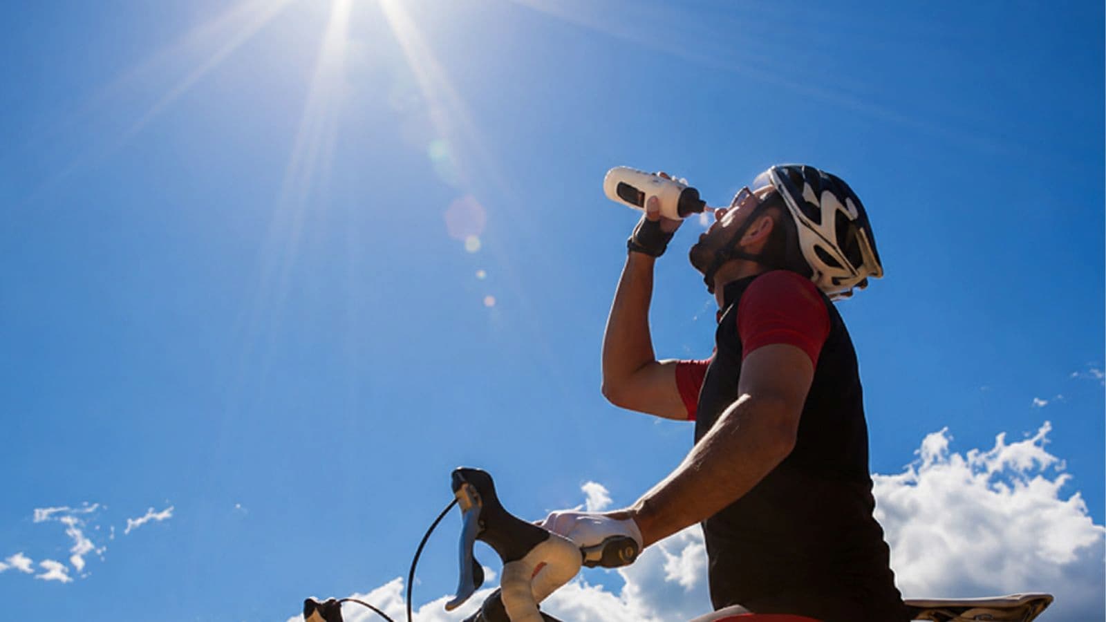 Triathlete drinking from a bottle while cycling in hot and sunny conditions during a long-distance triathlon.