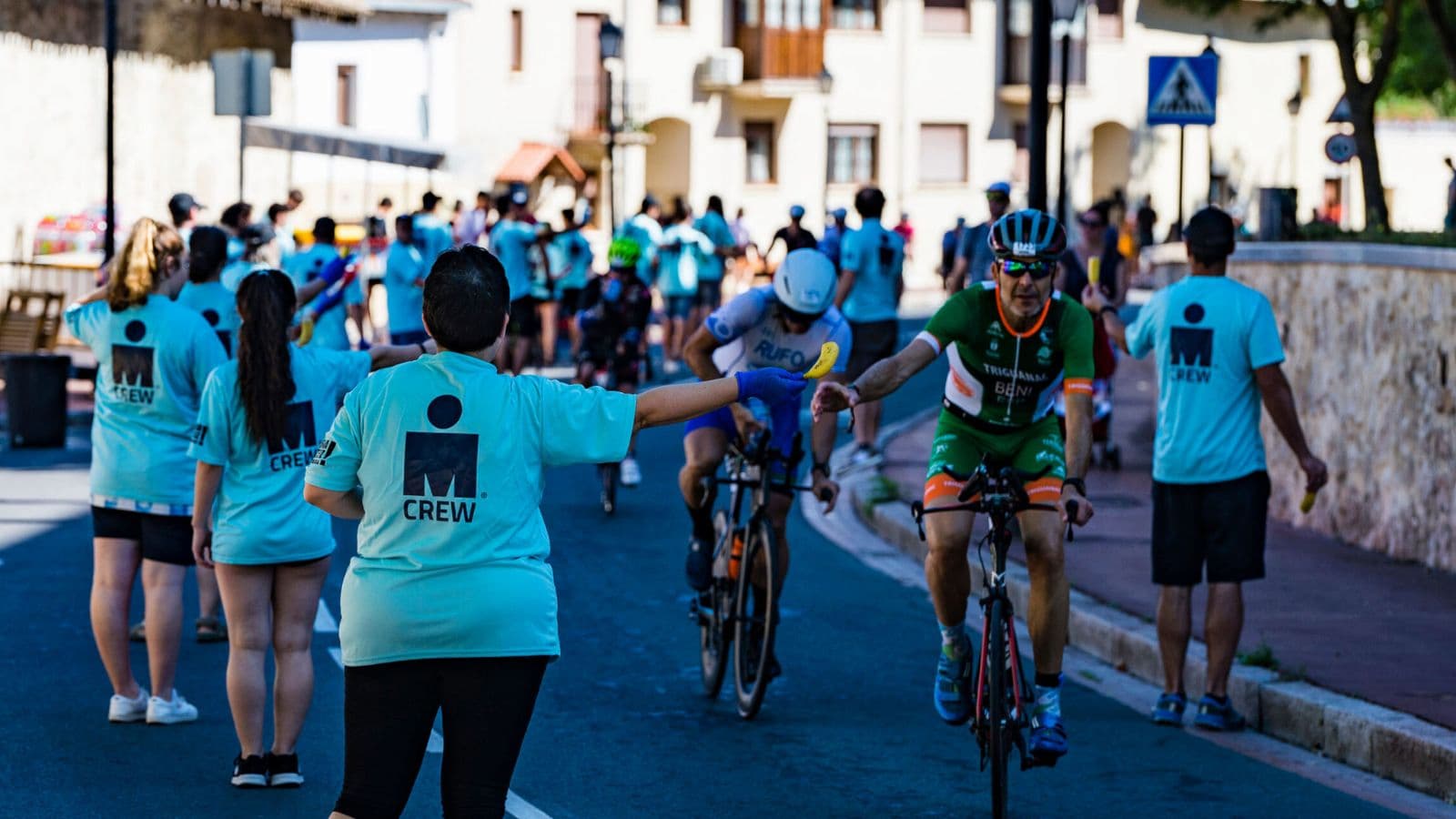 Triathlete safely collecting a hydration bottle from a volunteer while passing through an aid station during the bike leg of a triathlon.