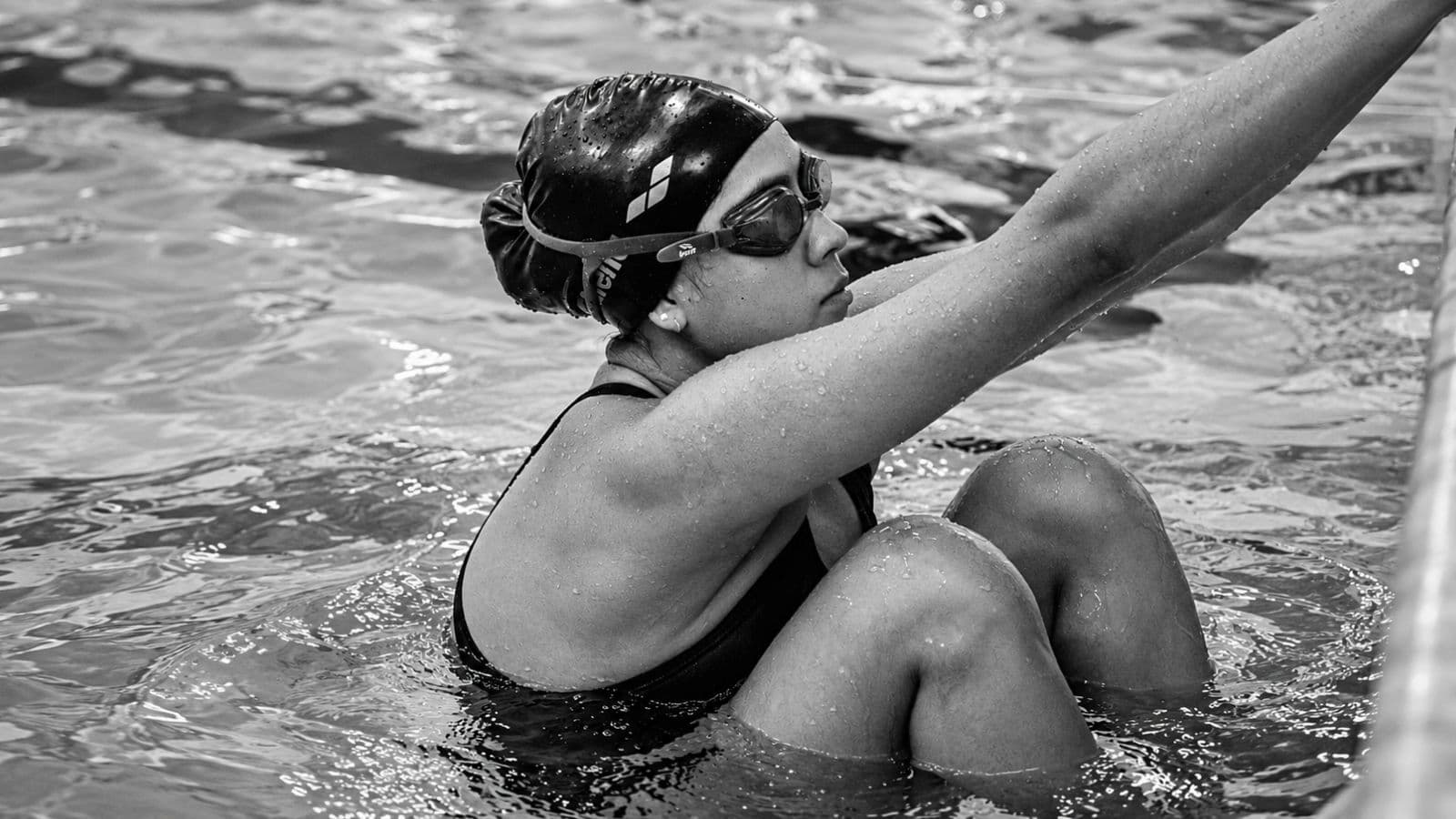 Triathlete sitting beside a swimming pool and holding the inner knee after experiencing discomfort during breaststroke training.