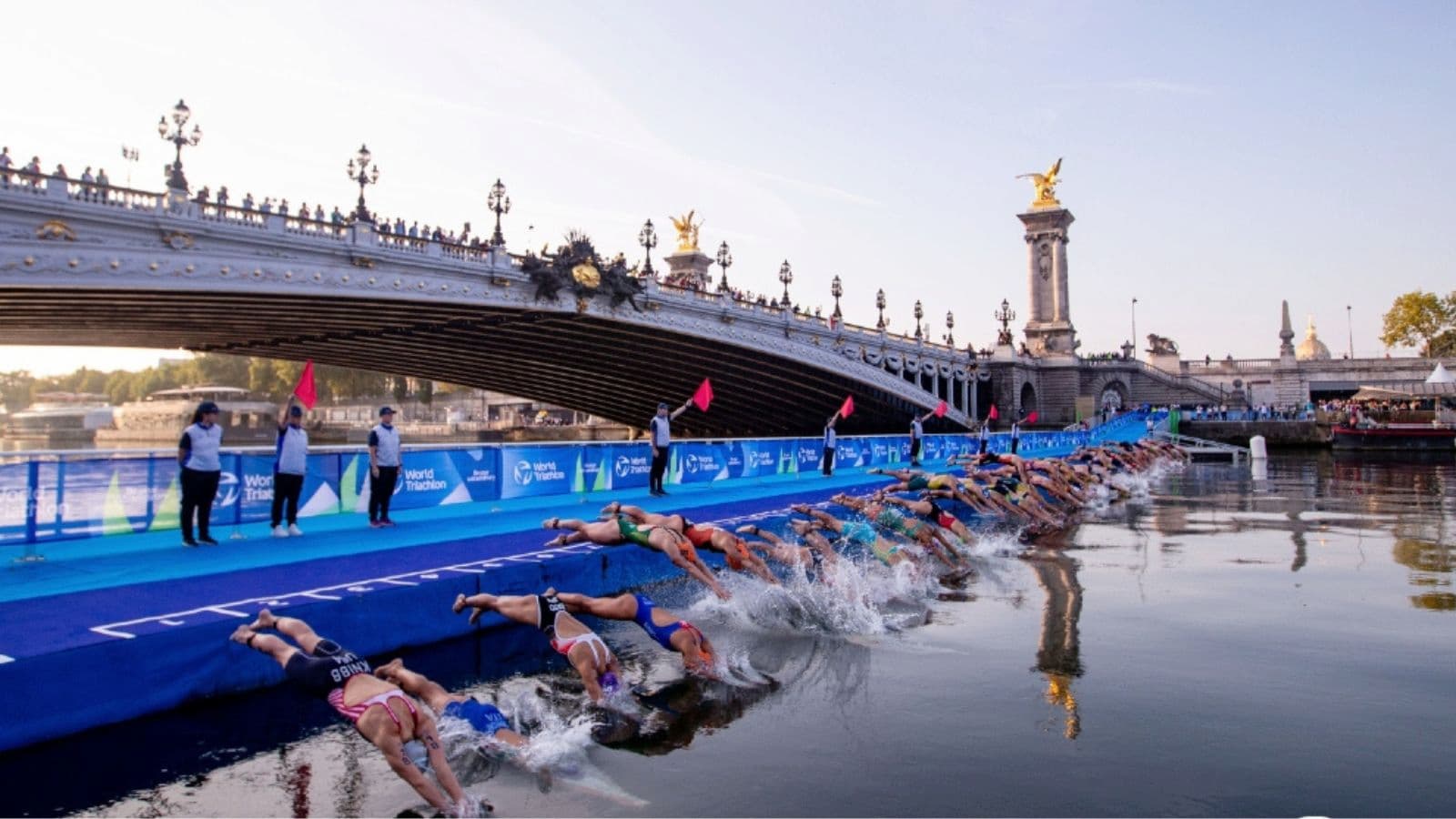 Triathletes performing a dolphin dive through shallow open water during the start of a triathlon swim.