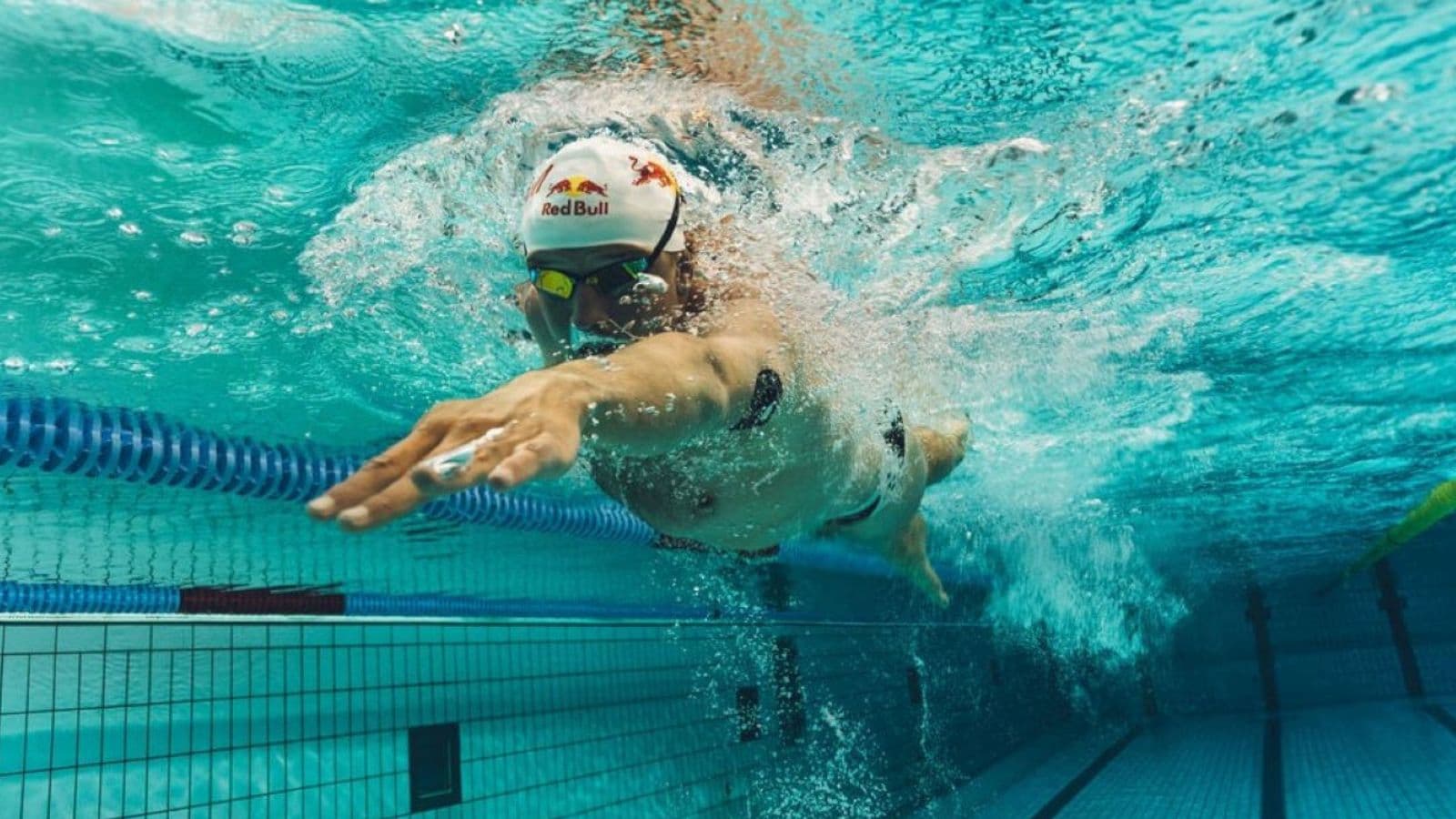 Triathlete checking swim time, distance, pace, and stroke data on a waterproof sports watch after completing a pool swimming workout.