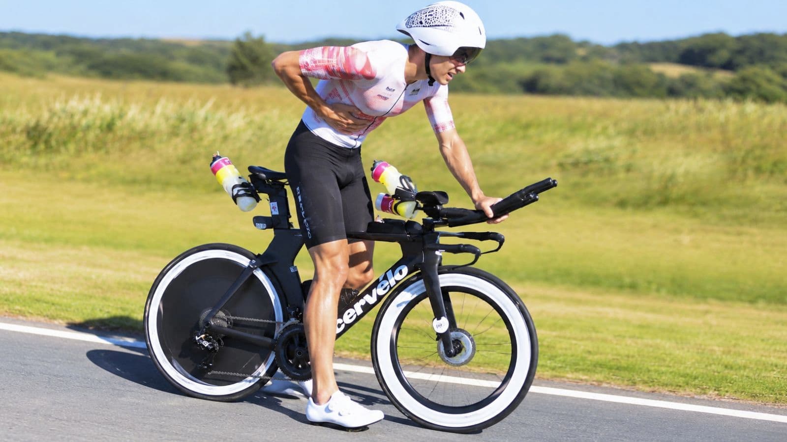 Road cyclist stopped beside a quiet cycling route, holding the side of their abdomen after experiencing a sudden side stitch during a ride.